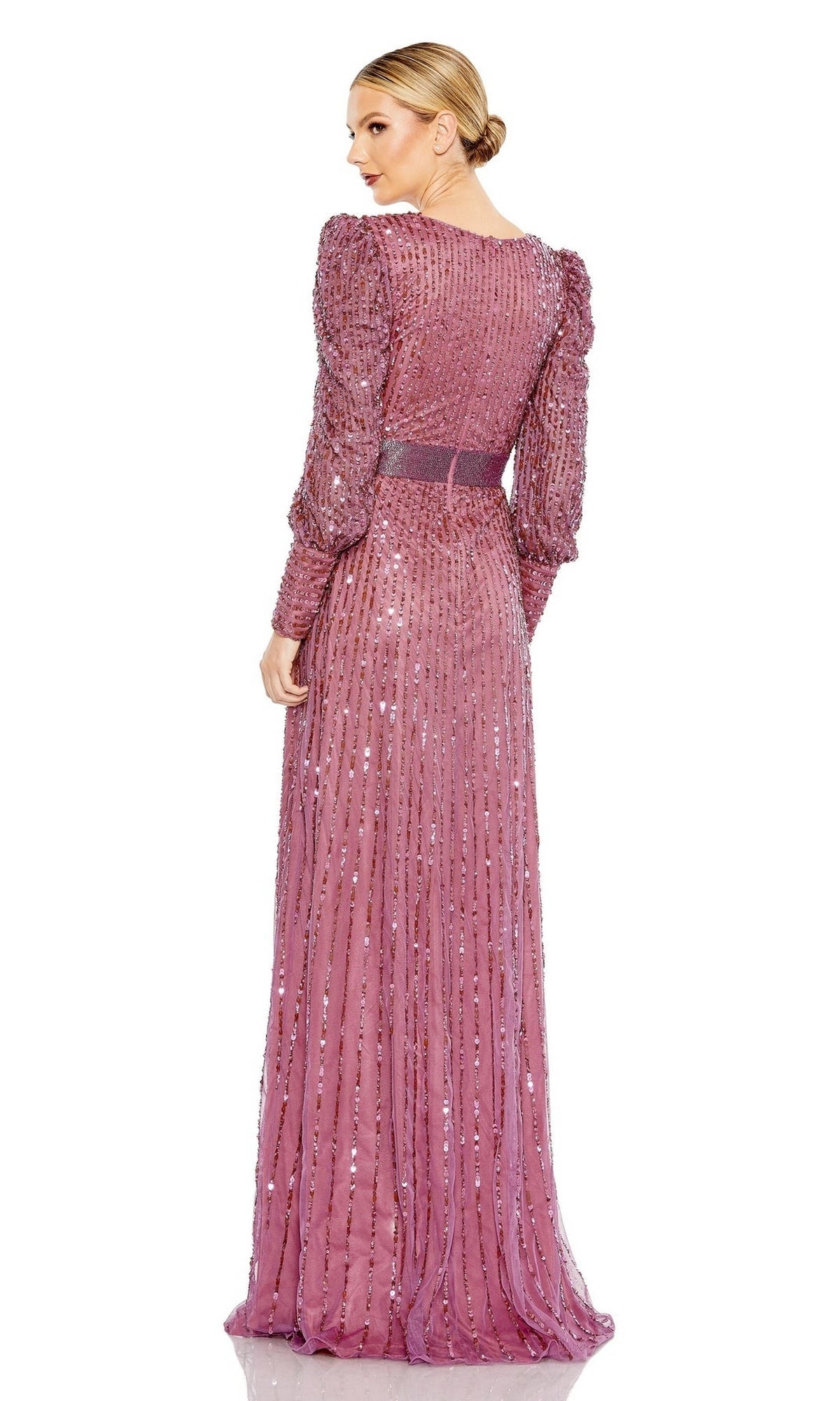 A woman stands facing away, her hair in a sleek bun, wearing the Mac Duggal 5720 long sleeve sequin formal dress in pink.
